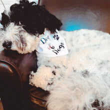 Load image into Gallery viewer, Cute and fluffy black and white doodle lying on a chair wearing a white bandana with multi-colored writing and a muddy paw print which reads "dog of dogs"
