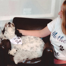 Load image into Gallery viewer, Cute and fluffy black and white doodle lying in a chair wearing a white bandana with multi-colored writing and a muddy paw print which reads &quot;dog of dogs&quot;, while a woman cuddles him and wears a matching white tee which reads &quot;Mother of dogs&quot;
